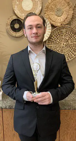 Person in suit with award, artistic wall.