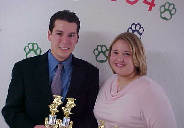 Two people holding trophies, smiling