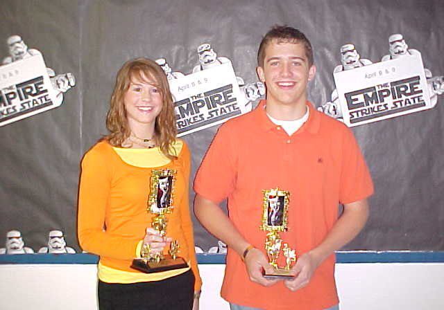 Two people holding trophies, smiling