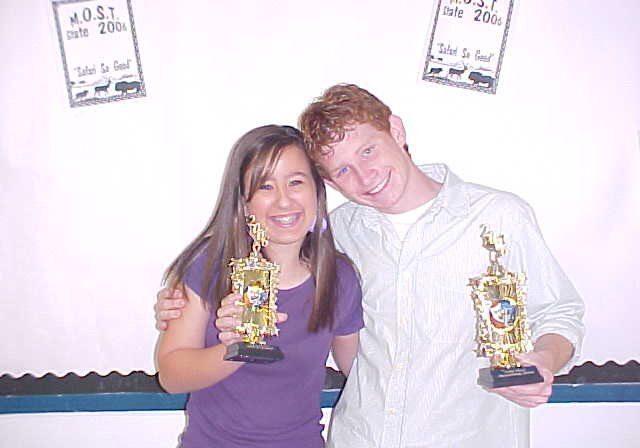 Two people smiling with trophies