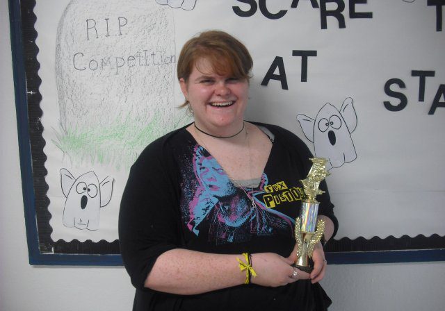 Woman with trophy in front of poster