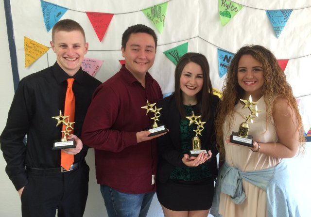 Four people with awards in front of banner