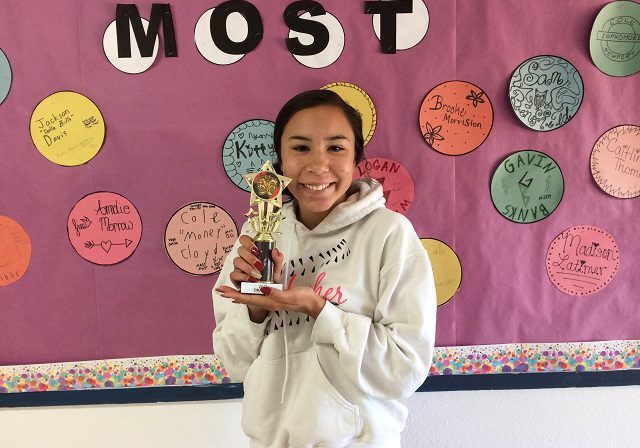 Student holding trophy, smiling in classroom