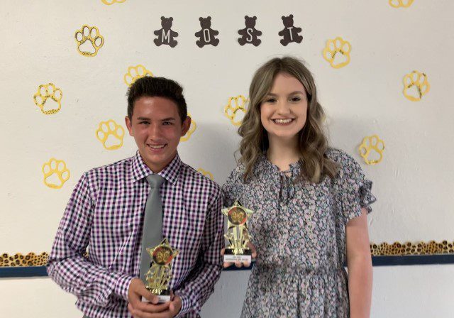 Two smiling people holding trophies