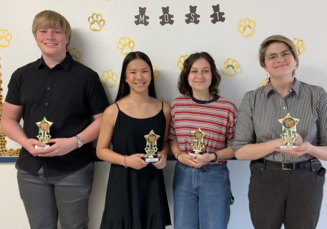 Students holding trophies in front of wall