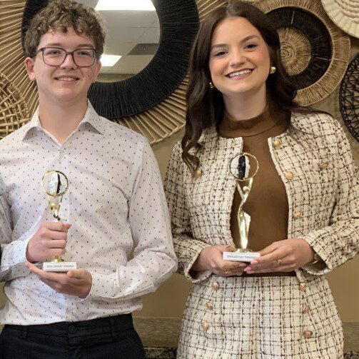 Two people holding trophies, smiling